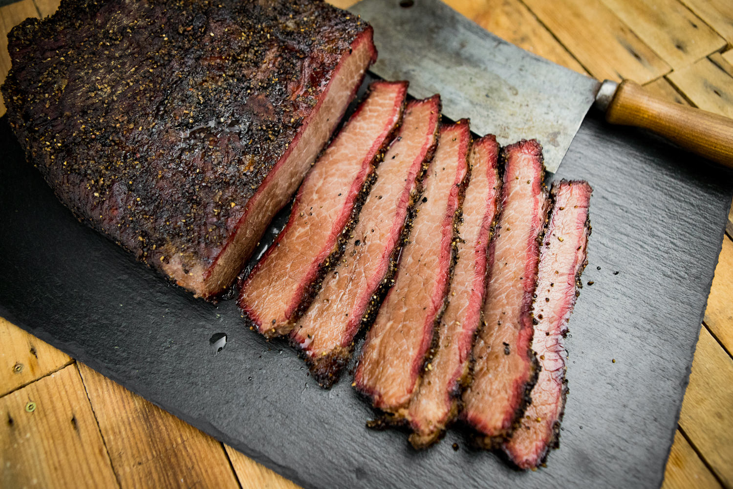 Brisket Paket von Oberpfalz Beef – Premium Rinderbrust kaufen Mehrere Scheiben saftig gegartes Rinderbrustfleisch (Brisket) mit aromatischer Kruste auf einem Holzbrett angerichtet, begleitet von rustikalem Besteck und Gewürzen – perfekte Zubereitung für BBQ-Liebhaber; Produktfoto des Oberpfalz Beef Brisket Pakets.