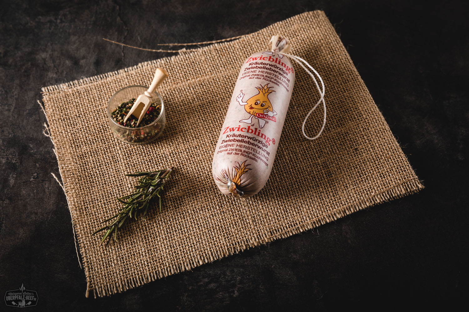 Zwiebling Portionswurst aus regionalem Rindfleisch – Frisch & vakuumverpackt kaufen Portionswurst „Zwiebling“ von Oberpfalz Beef, zwei kompakte, vakuumverpackte Würste aus hochwertigem Rindfleisch auf rustikalem Holzbrett mit Kräuterzweig, im Hintergrund dunkle Steinplatte – regionale Delikatesse, handwerklich hergestellt.