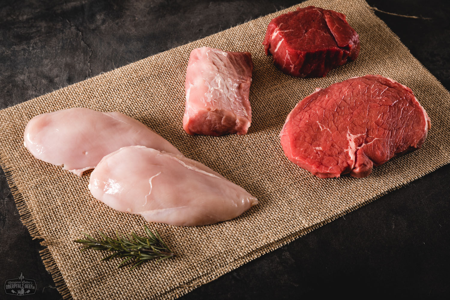 Fondue-Paket von Oberpfalz-Beef mit vielfältiger Auswahl an hochwertigem, rohem Rindfleisch auf schwarzem Tablett, umgeben von Dip-Schälchen, Gemüse, Kartoffeln und Brot – stilvoll angerichtet auf rustikalem Holztisch.