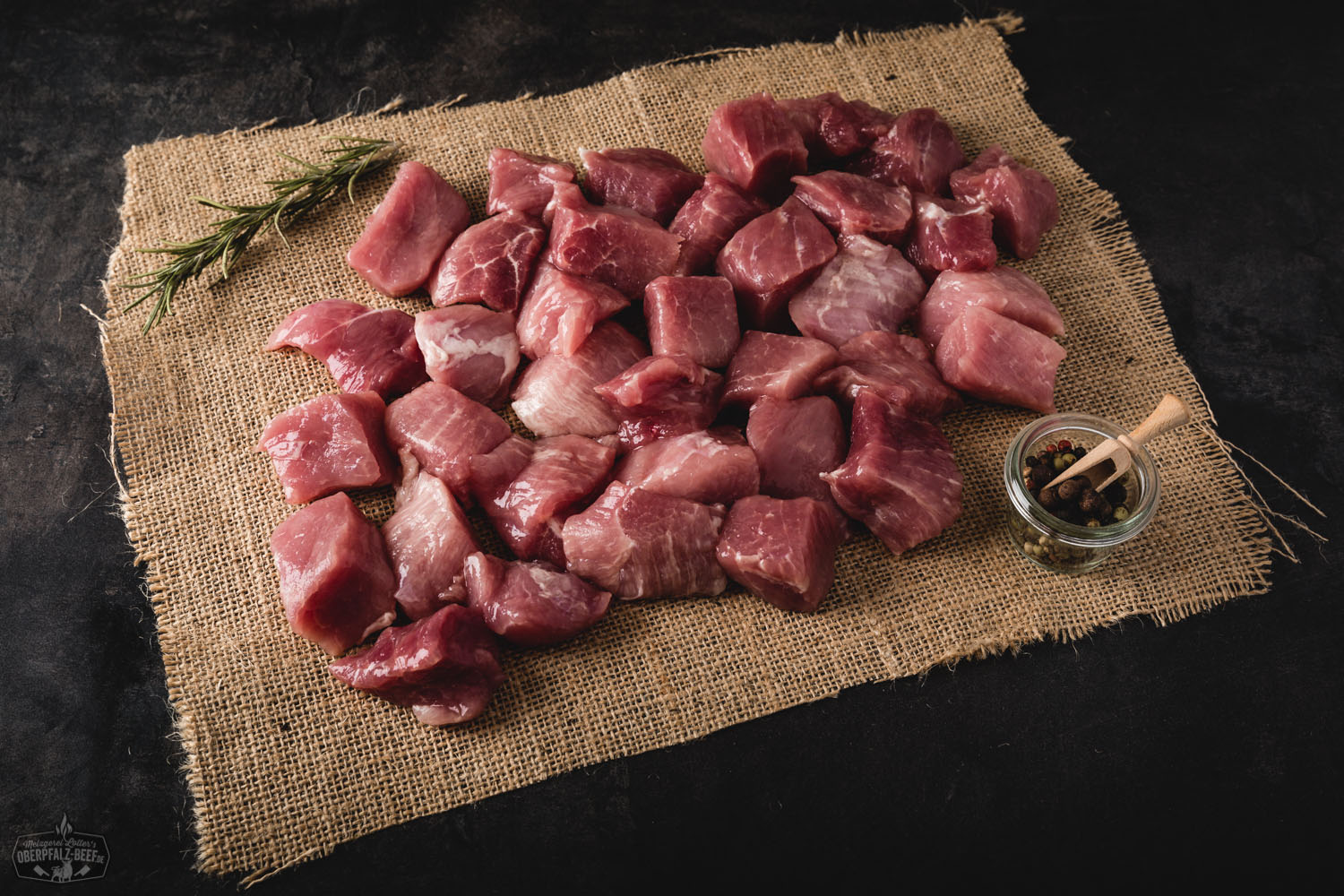 Handgeschnittenes Gulasch vom Oberpfälzer Landschwein – Frisches Schweinefleisch in Premium-Qualität Handgeschnittenes Gulasch vom Oberpfälzer Landschwein, roh und in gleichmäßige Stücke geschnitten, auf dunklem Holzuntergrund präsentiert – frisches Schweinefleisch aus regionaler Herkunft, ideal für deftige Schmorgerichte.