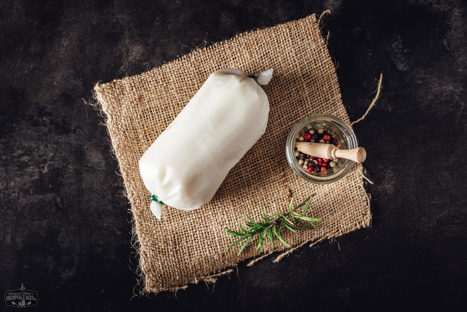 Ausgelassenes Schweinefett in Glas – naturbelassenes Schmalz aus der Oberpfalz Rohe Lammhüfte vom Juradistl-Lamm auf dunkler Schieferplatte, umgeben von Rosmarinzweigen, buntem Pfeffer, grobem Salz und Knoblauchzehen – hochwertige Fleischspezialität für bewusste Genießer.