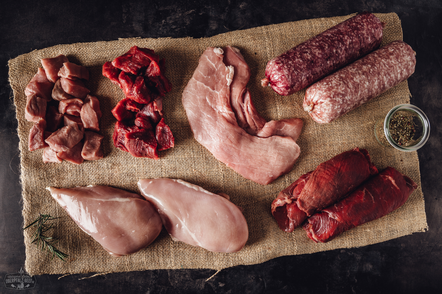 Bauernhof Fleischbox gemischt – Regionales Rindfleisch direkt vom Erzeuger Verschiedene vakuumverpackte Fleischstücke, darunter Rind, Schwein und Wurstwaren, liegen sortiert in einem offenen Pappkarton auf einem Holztisch – die Bauernhof-Box Mixed von Oberpfalz Beef mit regionalem Fleisch in Premiumqualität.