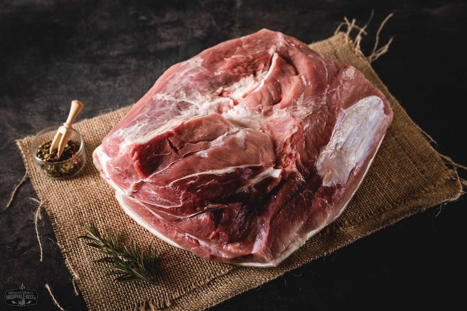 Backschinken gepökelt mit Schwarte vom Oberpfälzer Landschwein – regionales Qualitätsfleisch Rohes Pollo Fino vom Oberpfälzer Bauernhähnchen, ohne Knochen, auf einem dunklen Schneidebrett angerichtet, mit frischen Rosmarinzweigen, Meersalz und Pfefferkörnern garniert – ideale Zutat für saftige Hähnchenrezepte oder Grillgerichte.