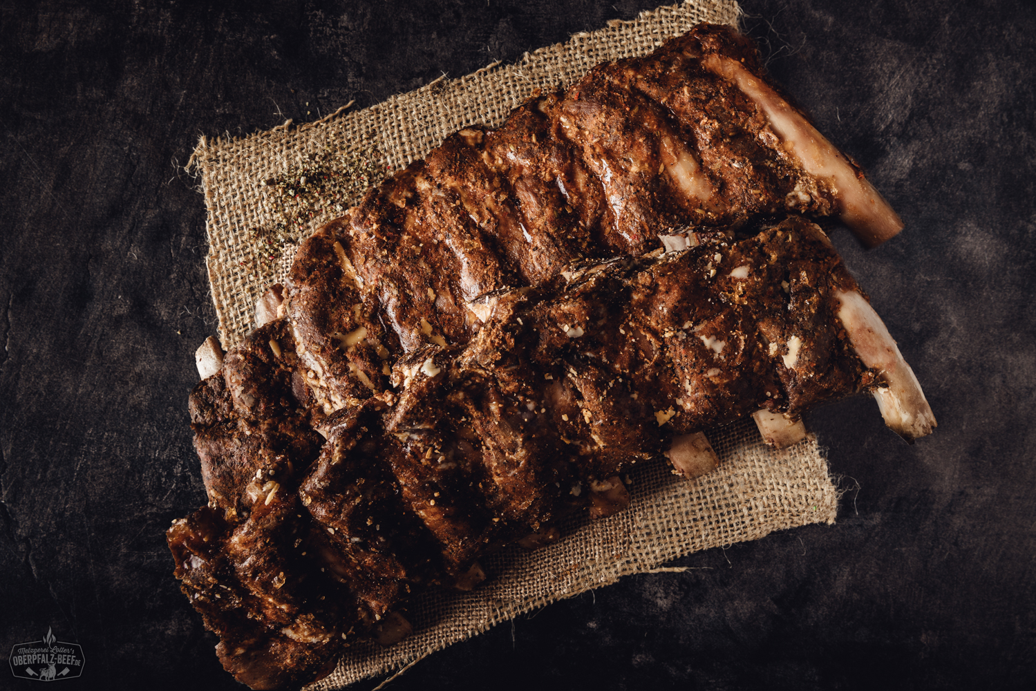 Sous-vide gegarte Beef Back Ribs vom Oberpfalz-Rind auf Schneidebrett mit BBQ-Sauce Sous-vide gegarte Beef Back Ribs vom Oberpfalz-Rind, saftig und zart mit dunkler BBQ-Glasur, angerichtet auf einem Holzbrett mit frischen Kräutern und Gewürzen, rustikaler Hintergrund – perfekte Grill-Delikatesse für Fleischliebhaber.