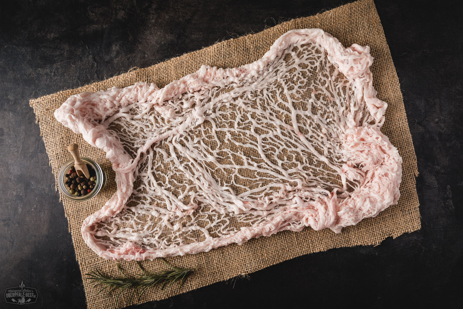 Netz vom Oberpfälzer Landschwein – Regionales Schweinefleisch in Metzgerqualität Rohes Stück Netzbraten vom Oberpfälzer Landschwein auf dunklem Untergrund, marmoriert und in feines Schweinenetz gehüllt, frisch und saftig mit sichtbarer Fettstruktur – hochwertiges regionales Schweinefleisch für Braten oder Schmoren.