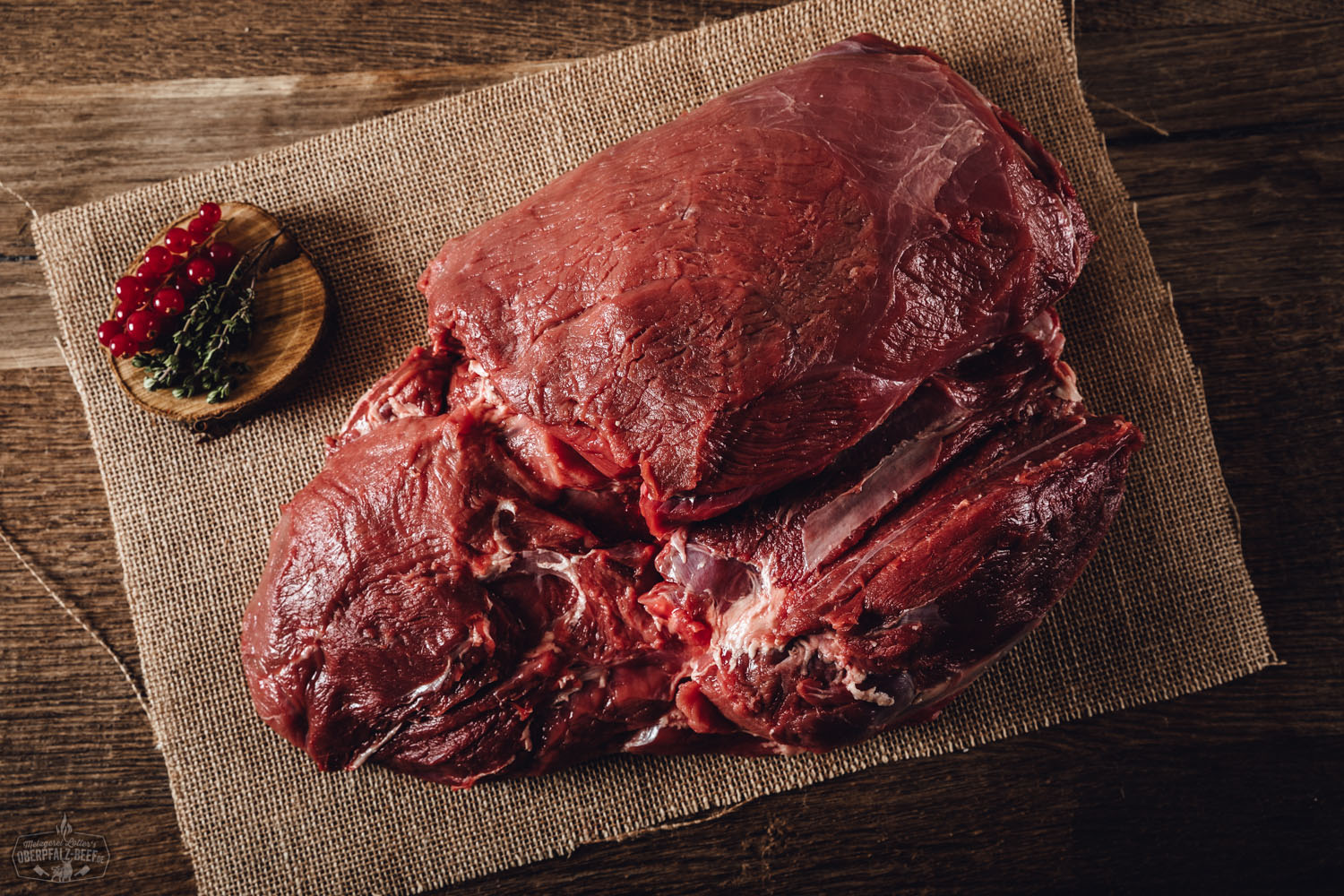 Roher Keulenbraten ohne Knochen vom Oberpfälzer Wildschwein auf Holzbrett, umgeben von Rosmarinzweigen, Wacholderbeeren und Meersalz – frisches, regionales Wildfleisch für natürliche Zubereitung.