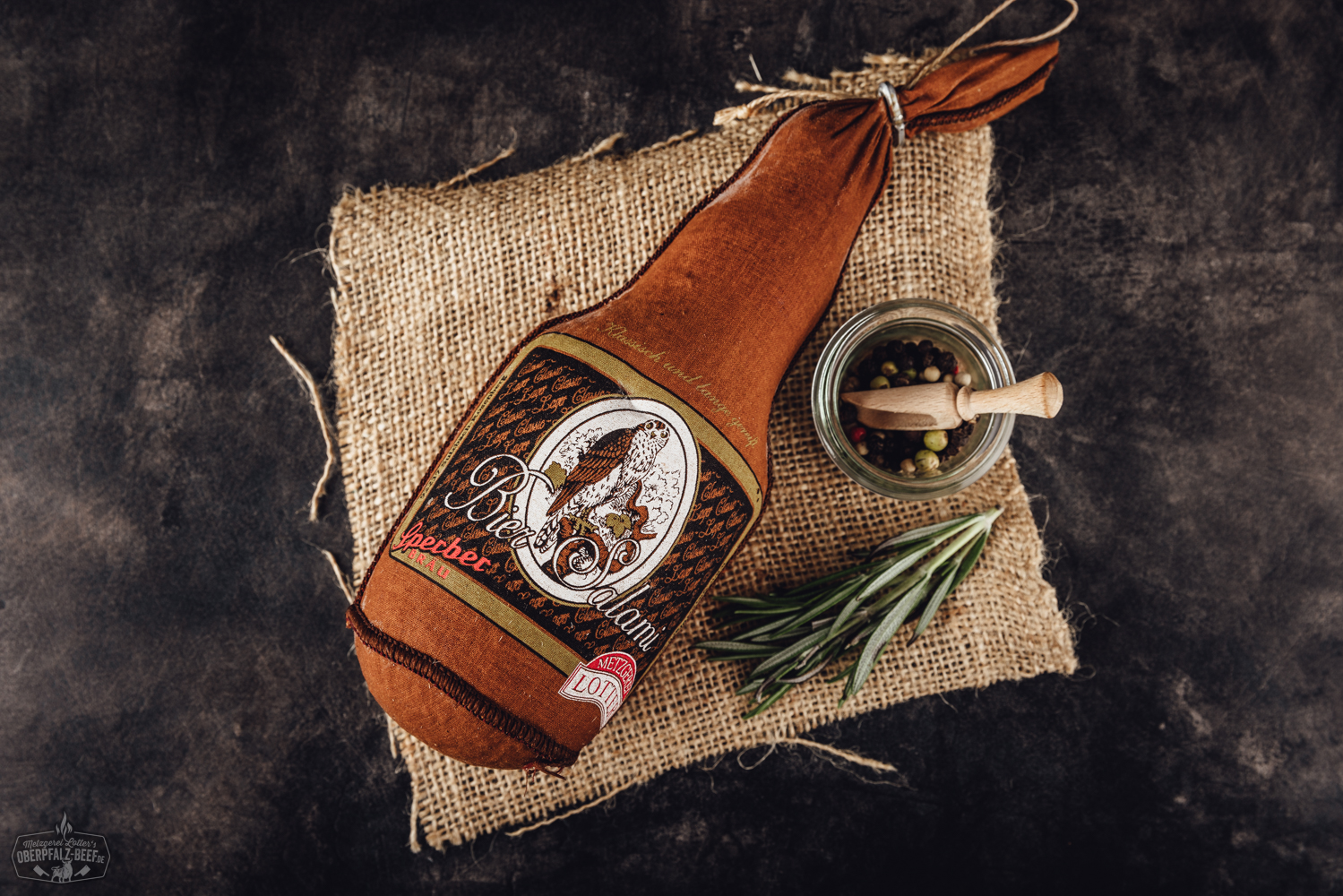 Biersalami aus Bayern – Hausgemachte Spezialität aus der Oberpfalz Nahaufnahme einer Biersalami auf einem Holzbrett mit angeschnittener Scheibe, umgeben von Pfefferkörnern und einem Bierglas im Hintergrund – hochwertige Delikatesswurst aus der Oberpfalz.