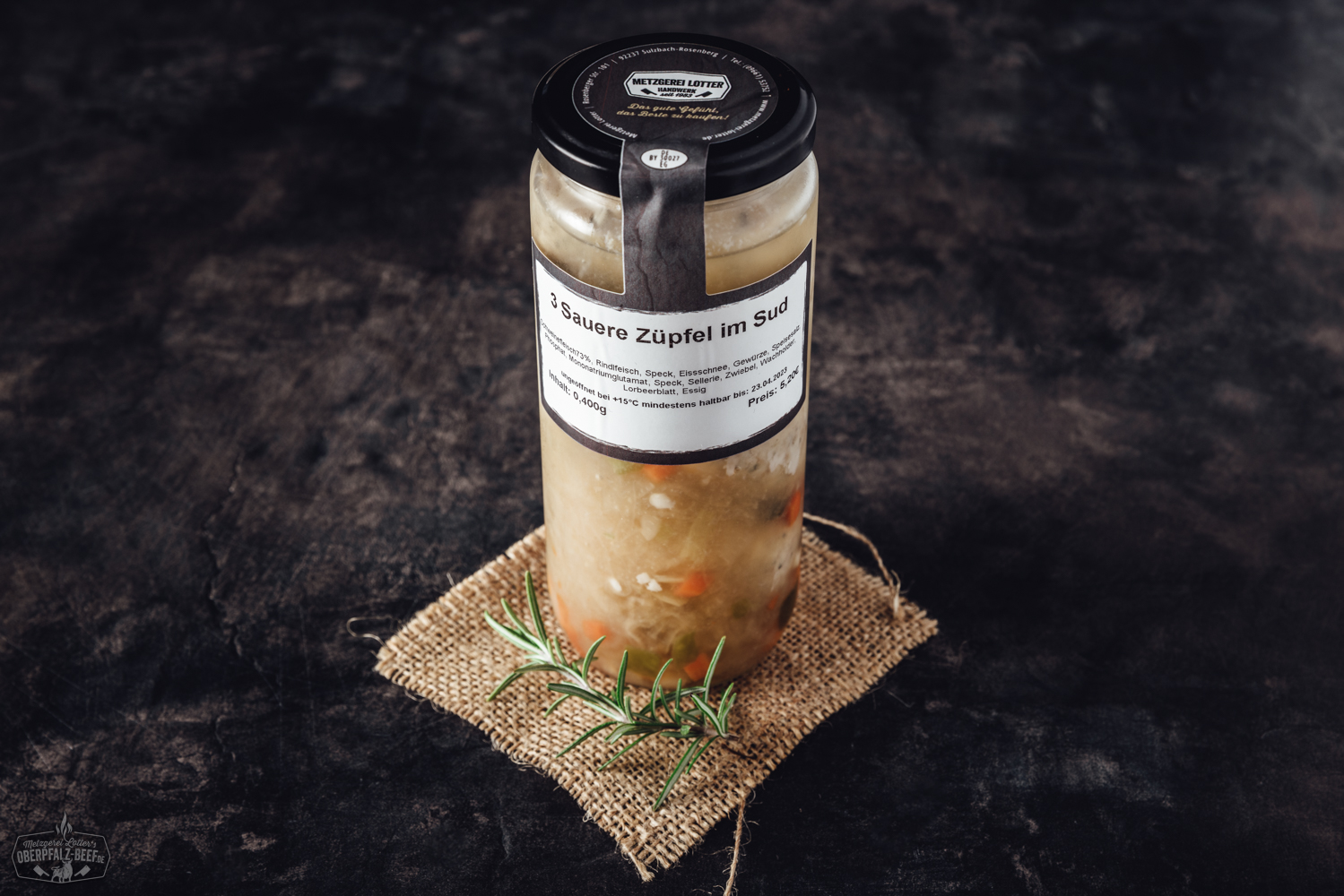 Traditionelles fränkisches Gericht „Saure Zipfel“: Zwei in Essigsud gegarte Bratwürste serviert mit Zwiebelringen in klarer Brühe auf einem weißen Teller, rustikale Präsentation auf dunklem Holzuntergrund – deftige regionale Spezialität aus Bayern.