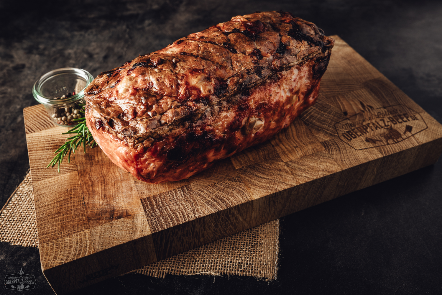 Kalbfleischleberwurst in Portionsgröße aufgeschnitten auf einem Holzbrett, dekoriert mit frischen Apfelscheiben, roten Zwiebelringen und Kräutern; traditionelle bayerische Wurstspezialität aus der Oberpfalz.