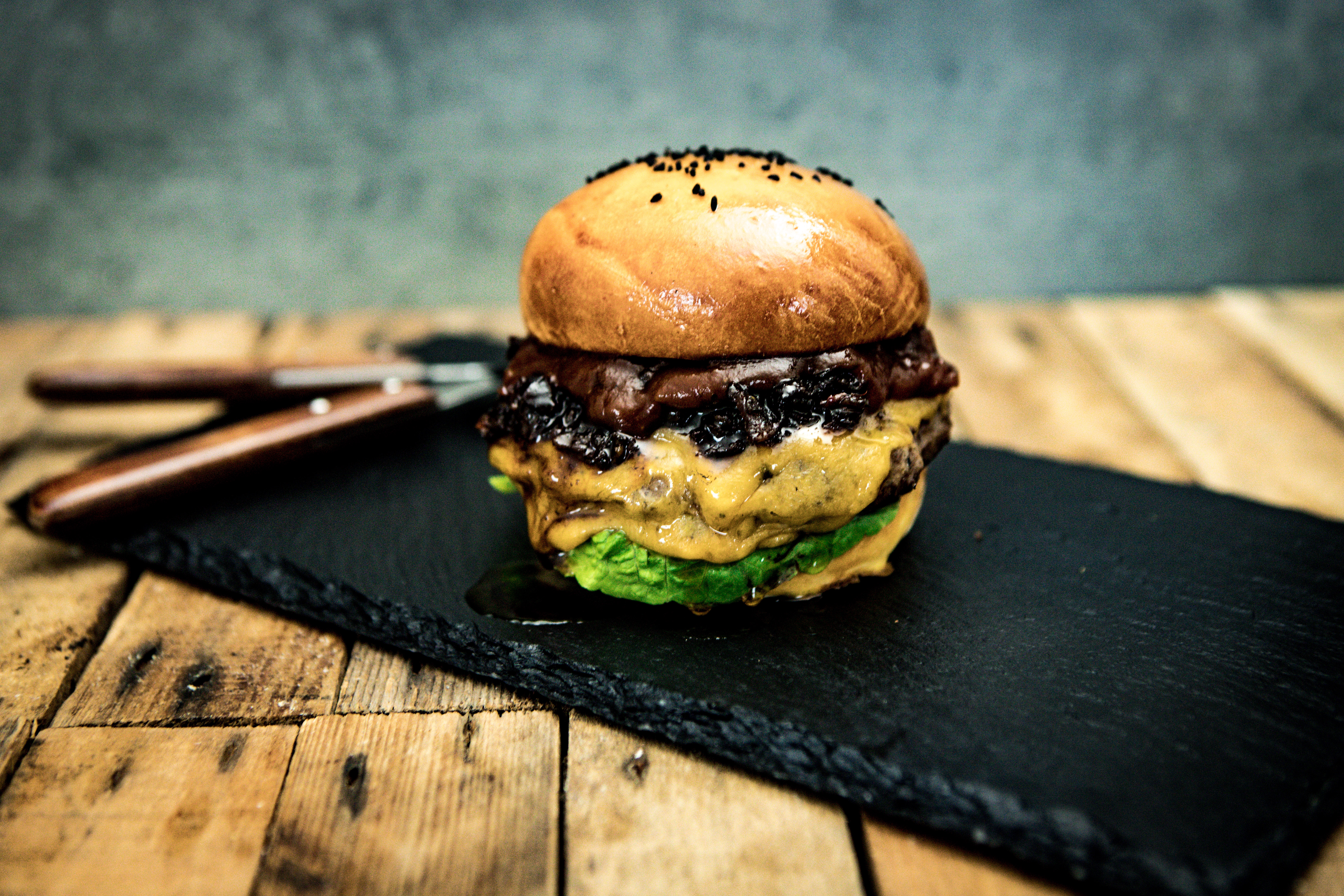 Wildburger mit frischem Salat und Tomate im rustikalen Brioche-Brötchen Nahaufnahme eines Wild-Burgers mit saftigem Wildfleisch-Patty, knackigem grünen Salat, roten Zwiebeln, geschmolzenem Käse und einer rustikalen Vollkorn-Burgersemmel, serviert auf einem Holzbrett – Burger im Gourmet-Stil für Wildfleischliebhaber.
