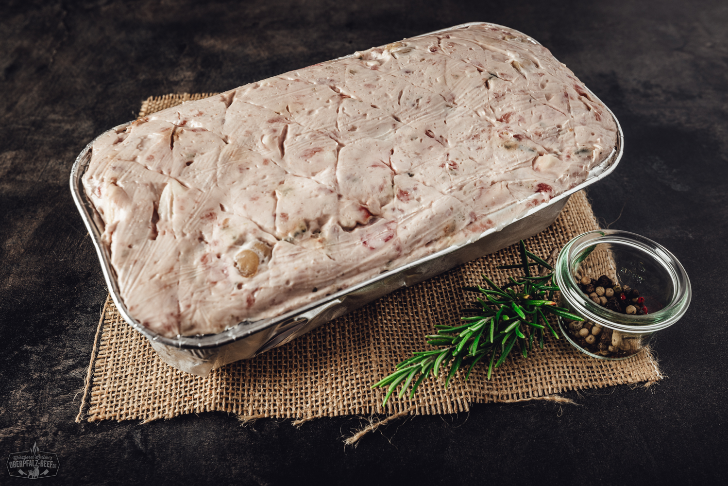 Kalbfleischleberwurst in Portionsgröße aufgeschnitten auf einem Holzbrett, dekoriert mit frischen Apfelscheiben, roten Zwiebelringen und Kräutern; traditionelle bayerische Wurstspezialität aus der Oberpfalz.