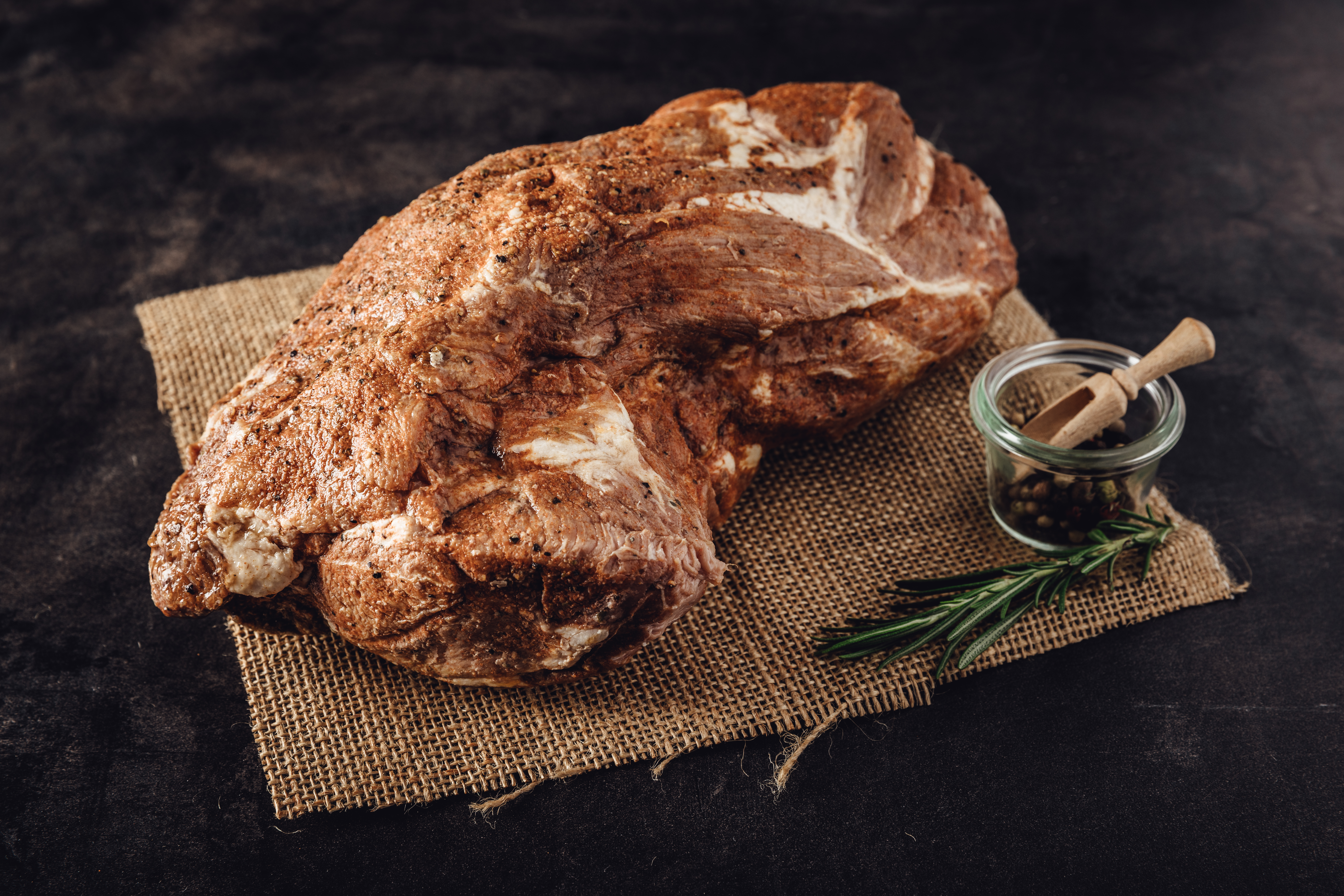Schweinebraten aus dem Hals - Rezept und Zubereitungstipps Bild eines saftigen Schweinebratens aus dem Hals, perfekt gebräunt und appetitlich auf einem Holzbrett angerichtet, umgeben von frischen Kräutern, ideal für traditionelle bayerische Küche und Fleischliebhaber.