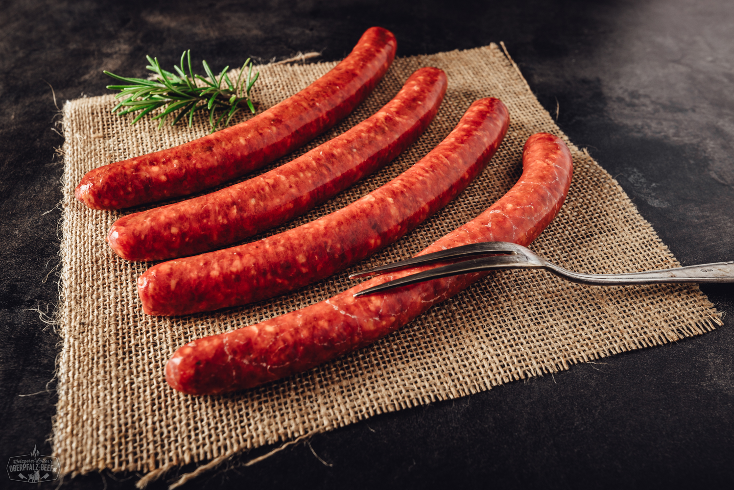 Merguez Bratwürste aus 100% Rindfleisch – würzig, hausgemacht und grillfertig Zwei goldbraun gegrillte Chili-Bratwürste mit sichtbaren Gewürzen liegen auf einem schwarzen Grillrost; im Hintergrund rote Chilischoten und Holzkohle – deftige Spezialität für Grillliebhaber.