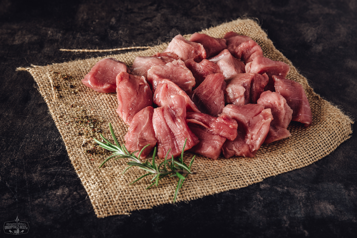 Handgeschnittenes Schweinefilet für Fondue, roh und in feine Scheiben geschnitten, appetitlich auf einem dunklen Brett angerichtet, daneben frische Kräuter und Gewürze – hochwertiges Fondue-Fleisch aus der Oberpfalz.