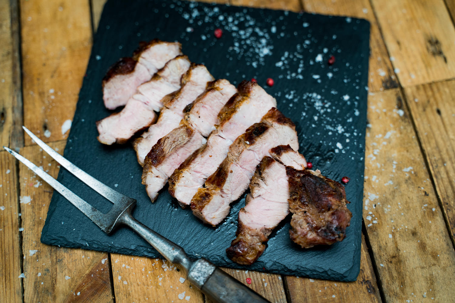 Gewürzte Halssteaks vom Rind auf Holzbrett – Frisches Grillfleisch kaufen Zwei saftig gewürzte Rinderhalssteaks liegen nebeneinander auf einem dunklen Schneidebrett, umgeben von grobem Salz, buntem Pfeffer, frischen Kräutern und Knoblauchzehen – ideal für Grillfans und Fleischliebhaber.