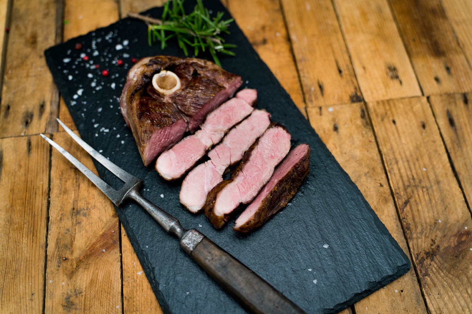 Steaks aus der Lammkeule vom Juradistl-Lamm frisch gegrillt auf Holzbrett Aufgeschnittener, saftiger Lammlachs-Rollbraten mit Kräuterkruste, perfekt gegart im Sous-vide-Verfahren, angerichtet auf einem Holzbrett mit Rosmarinzweigen und Gewürzen – hochwertiges Premium-Lammfleisch aus der Oberpfalz.