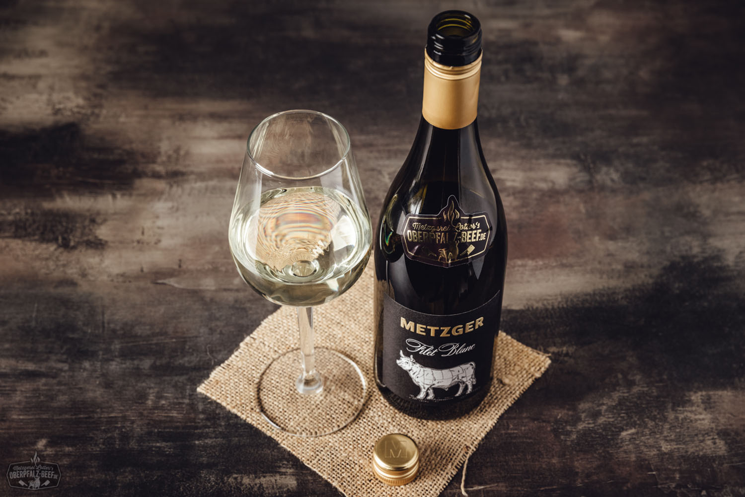 Porträt eines lächelnden Metzgers mit weißer Schürze, weißem T-Shirt und Kappe vor der Tür einer Metzgerei mit "Beef Buddy"-Logo – authentisches Handwerksbild für regionale Fleischqualität aus der Oberpfalz.