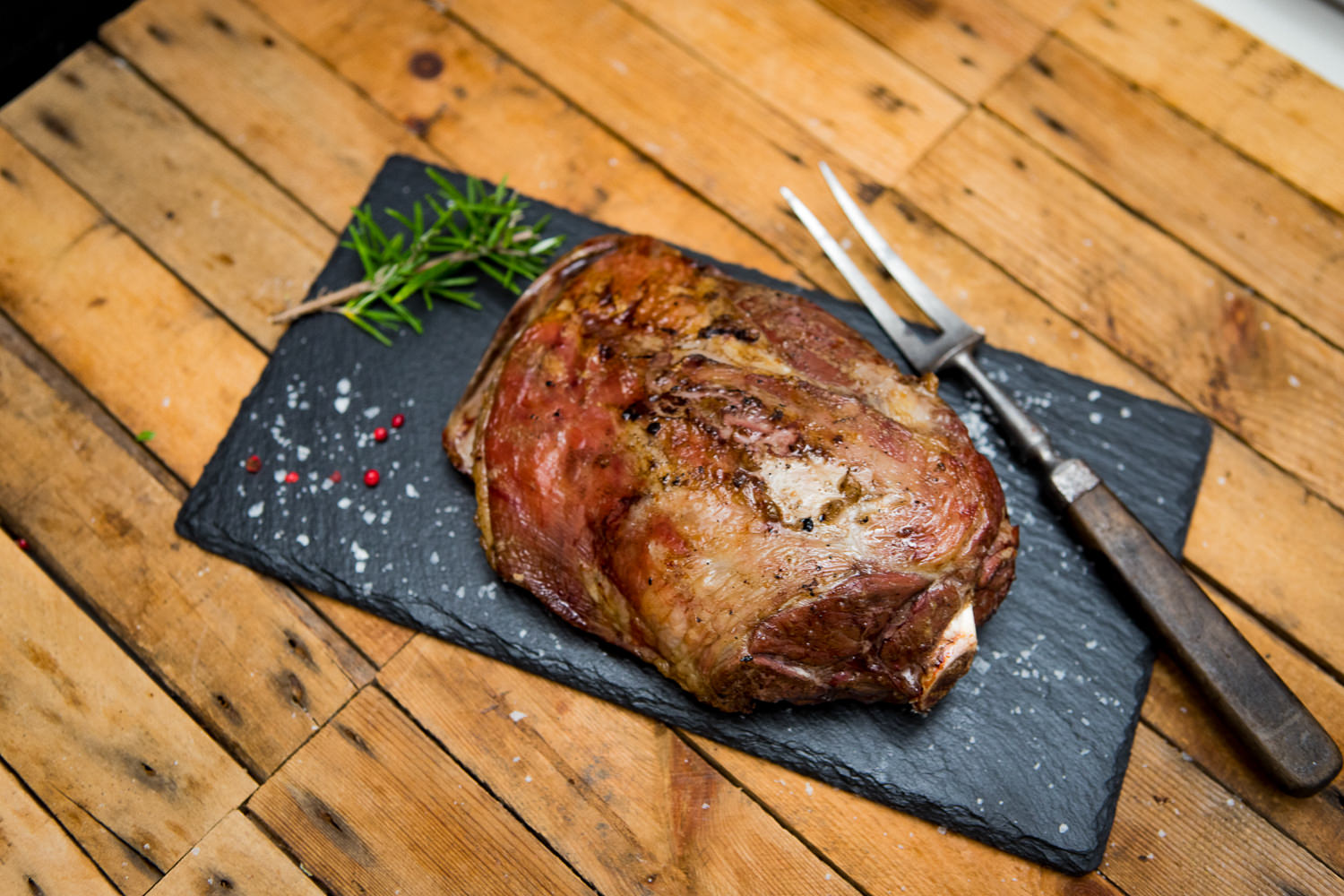 Lammschulter mit Knochen vom Juradistl Lamm – nachhaltig & regional aus der Oberpfalz Rohe Lammschulter mit Knochen vom Juradistl-Lamm auf dunklem Untergrund, seitlich angerichtet mit frischen Kräutern, Knoblauchzehen, Pfefferkörnern und einem Messer – hochwertige Fleischspezialität für Braten oder Schmoren.