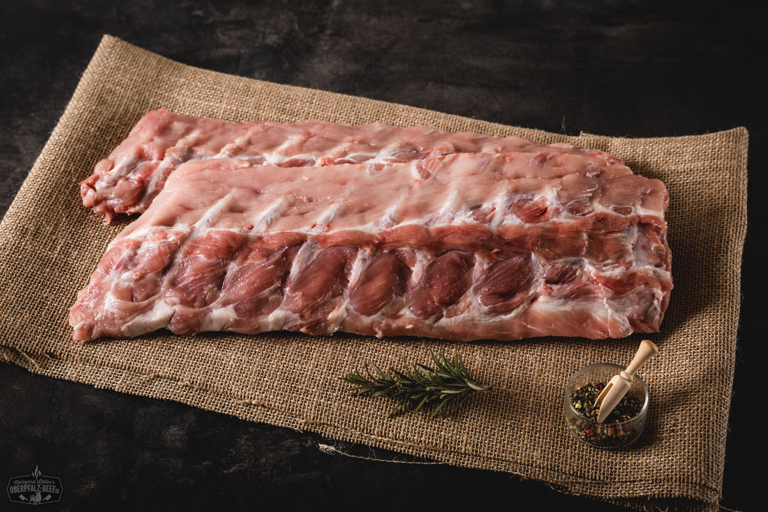 Kotelett Rippchen vom Oberpfälzer Landschwein, saftig und zart gegrillt auf einem Holzkohlegrill, mit goldbrauner Kruste und mariniertem Rosmarinzweig, perfektes bayerisches Grillfleisch.