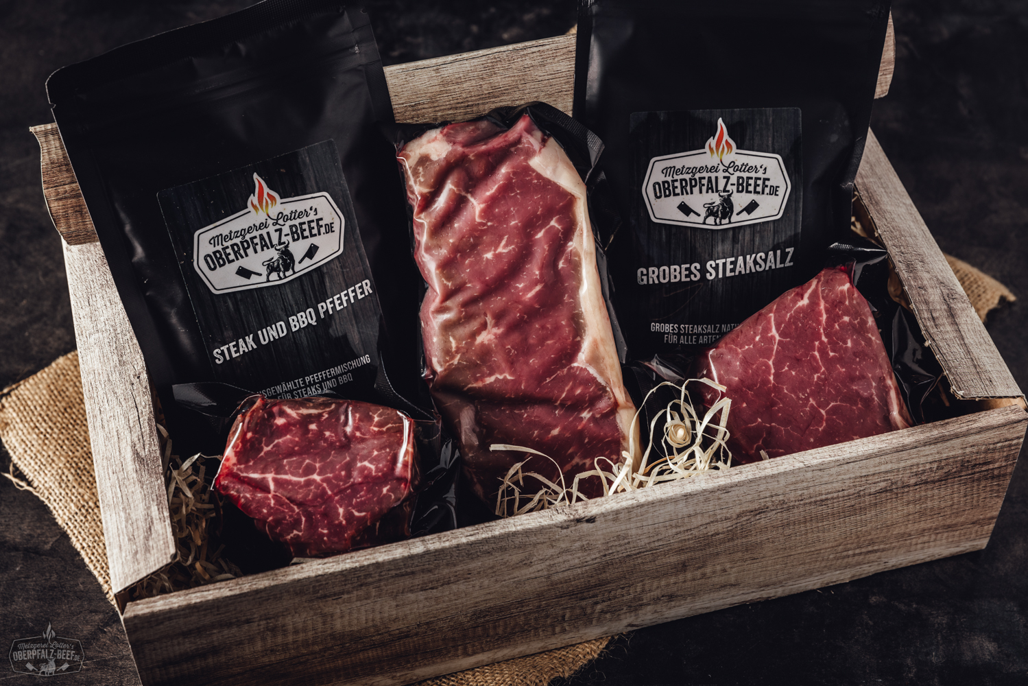 Nachhaltige Weihnachtsgeschenktasche aus Jute mit Rentier-Motiv Weihnachtlich dekorierte Papiertüte mit „Oberpfalz Beef“-Logo, gefüllt mit regionalen Fleischspezialitäten, auf Holztisch vor Tannenzweigen und roten Christbaumkugeln – stimmungsvolle Präsentation regionaler Feinkost zu Weihnachten.