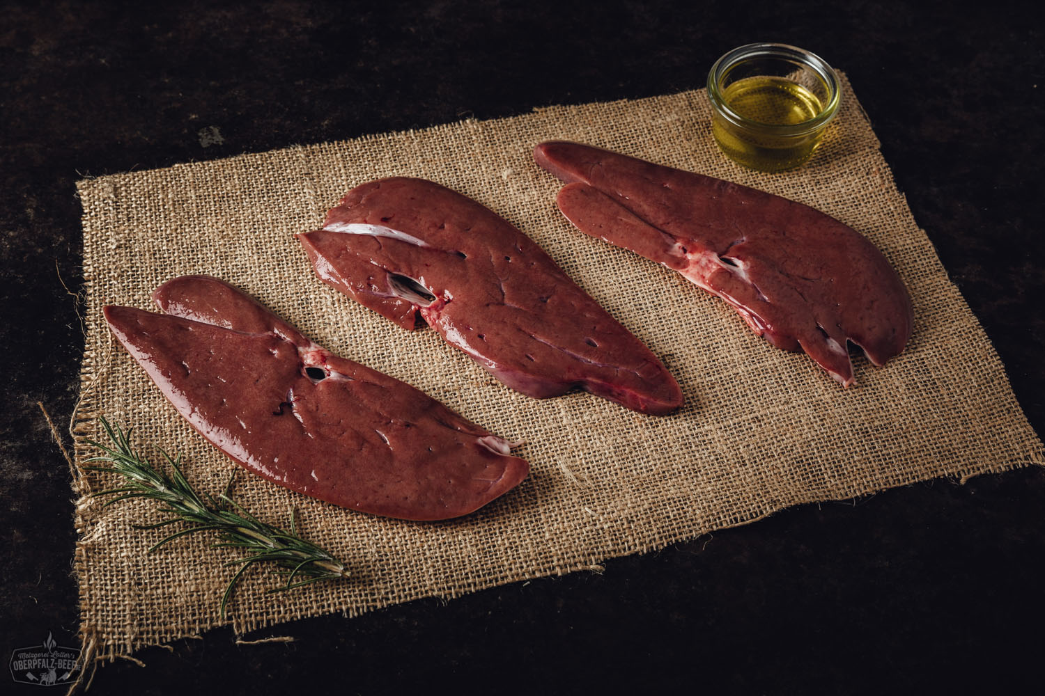 Leber in Scheiben vom Oberpfälzer Landschwein – Frisch und regional kaufen Roh geschnittene Schweineleber vom Oberpfälzer Landschwein, frisch angerichtet auf Holzbrett mit dunklem Hintergrund, detailreich sichtbare Fleischstruktur und kräftige Farbe, Darstellung hochwertiger regionaler Fleischqualität für bewusste Ernährung.