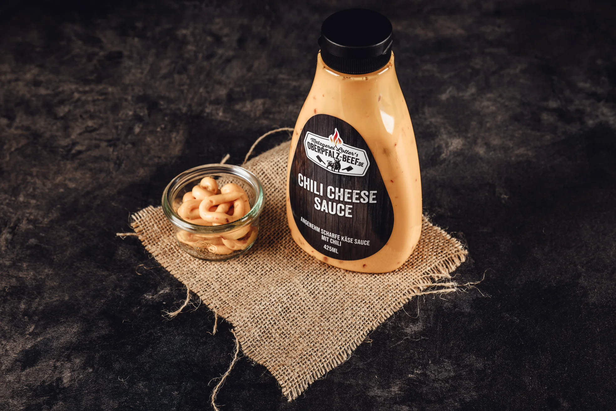 Chili-Cheese-Soße in Schale – würzige Käsesauce mit Jalapeños Nahaufnahme von zart geschmortem Kalbsbäckchen auf heller Keramikplatte, angerichtet mit dunkler Bratensauce, Wurzelgemüse und frischen Kräutern; hochwertige Fleischspezialität aus der Oberpfalz, perfekt gegart und servierfertig.