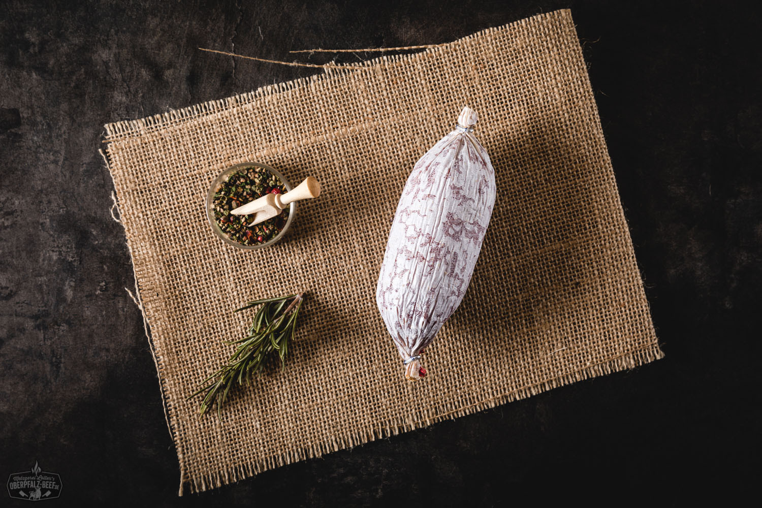 Nahaufnahme eines perfekt gegrillten Rindersteaks mit Pfefferkruste auf einem Holzbrett, umgeben von frischen Rosmarinzweigen, Meersalz und buntem Pfeffer – Oberpfalz Beef Premiumqualität für echten Fleischgenuss.