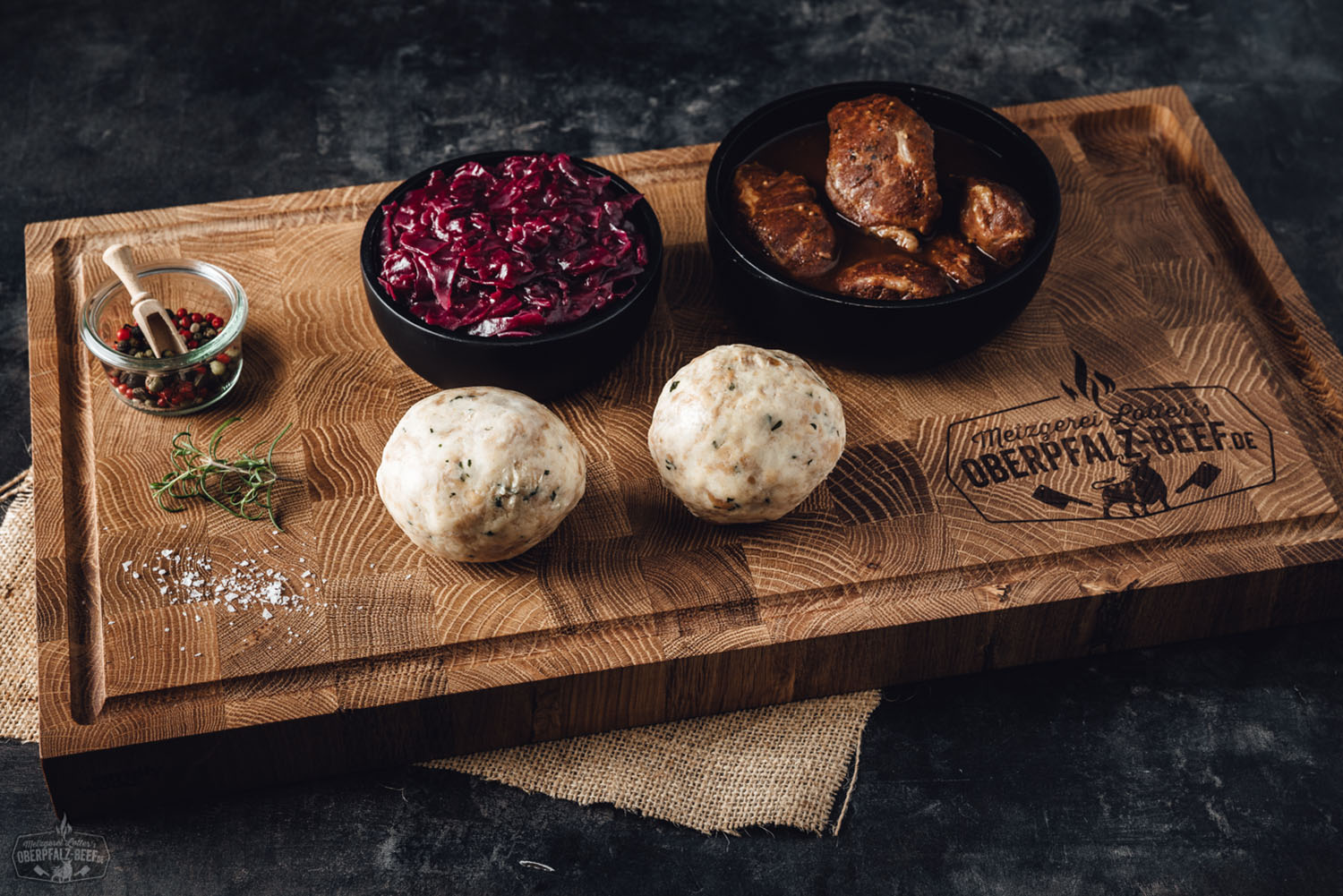 Oberpfälzer Schweinebacken Box – Premium Fleischqualität online bestellen Zwei gegarte Schweinebäckchen liegen in einer braunen Bratensauce auf einem weißen Teller, begleitet von cremigem Kartoffelpüree und glasierten Karotten; rustikal angerichtet auf dunklem Holzuntergrund – typisch bayerische Spezialität aus der Oberpfalz.