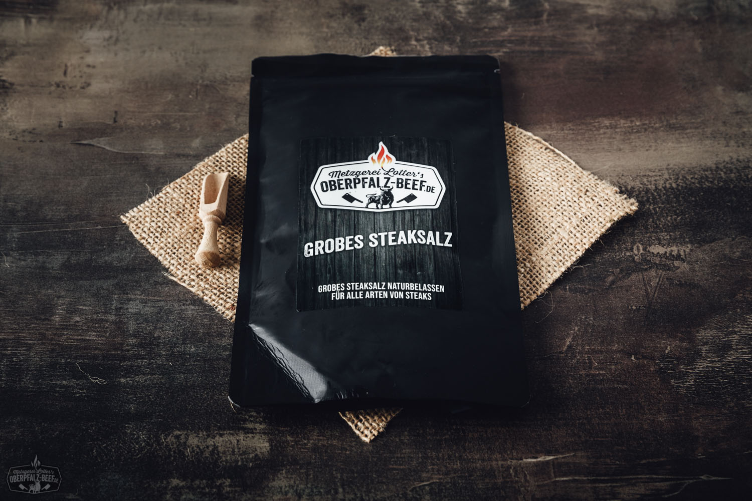 Glasbehälter mit grobem BBQ-Salz von Oberpfalz Beef auf dunklem Untergrund, daneben Kräuterzweig und grobes Salz verstreut – hochwertige BBQ-Zutat für Fleischliebhaber, Produktfoto für Grillgewürze und Rindfleisch-Veredelung.