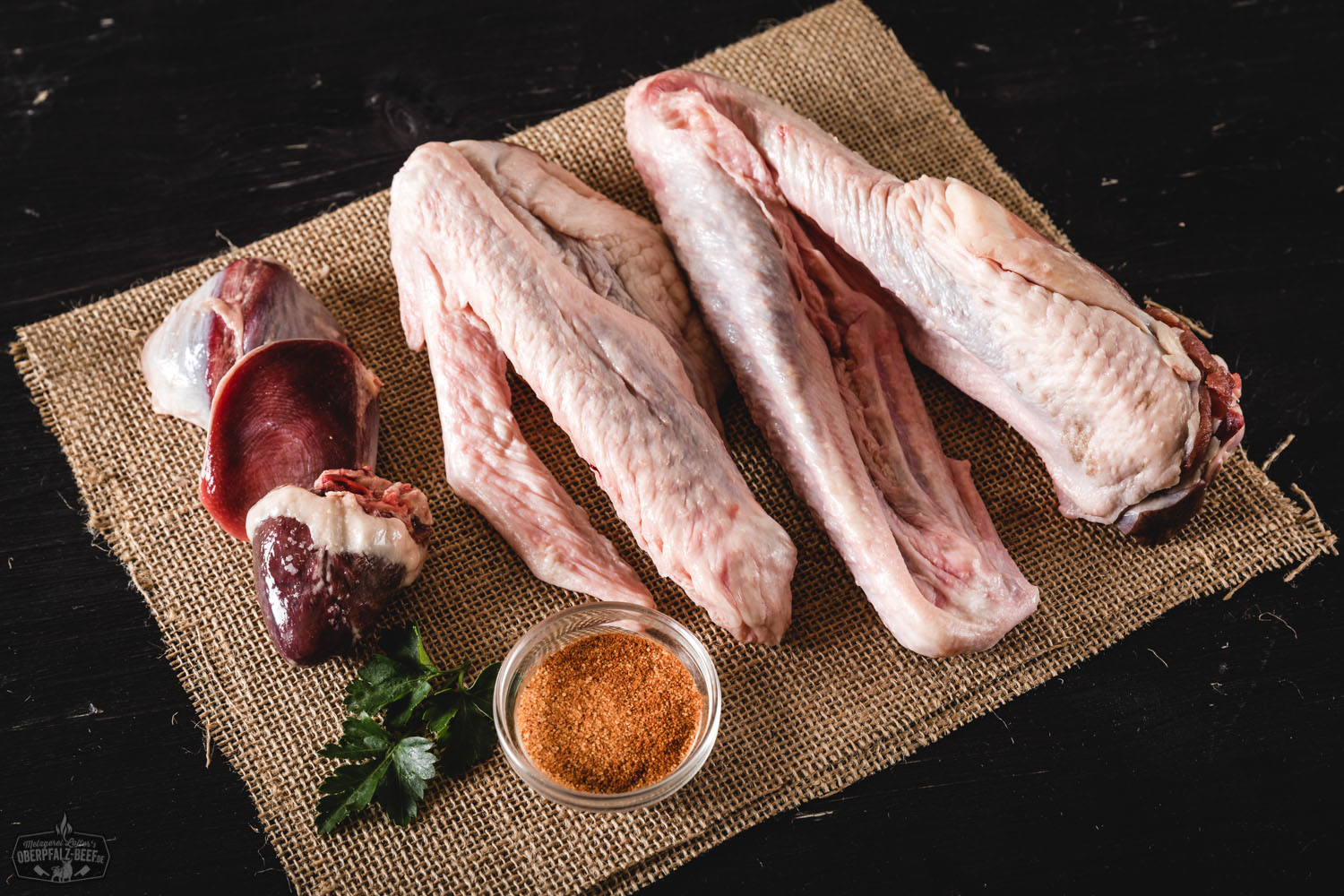 Kleinfleisch von der Oberpfälzer Bauerngans – Regionales Gänsefleisch aus artgerechter Haltung Frisches, rohes Gänsekleinfleisch von der Oberpfälzer Bauerngans auf einem rustikalen Holzbrett angerichtet, umgeben von Gewürzen, Kräutern und Gemüse, ideal zur Zubereitung von Suppen und Brühen – regionales Bio-Geflügel aus nachhaltiger Aufzucht.