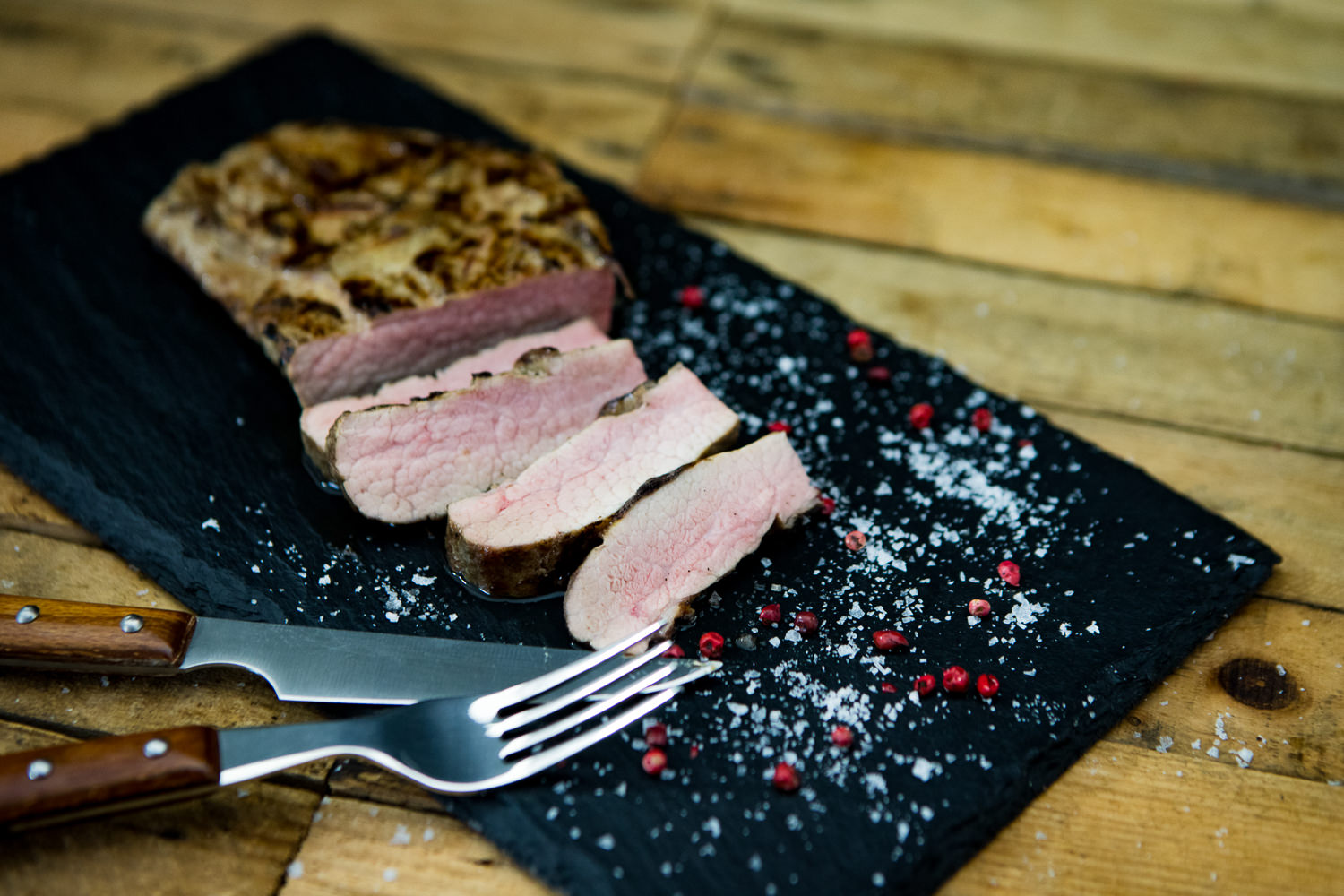 Pluma vom Oberpfälzer Landschwein perfekt gegrillt auf Holzbrett mit Kräutergarnitur Rohes Pluma-Steak vom Oberpfälzer Landschwein auf dunklem Untergrund, mariniert mit Kräutern und Gewürzen, garniert mit Rosmarin und Knoblauch – hochwertiges Schweinefleisch für Grill oder Pfanne.