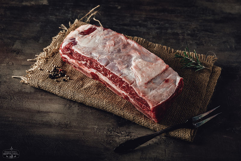 Portionsstück Short Ribs dry aged vom Oberpfalz-Rind, roh auf dunkler Oberfläche angerichtet; gut marmoriertes Rindfleisch mit sichtbarer Knochenstruktur, hochwertig und frisch, ideales BBQ-Fleisch für Grill oder Slow Cooking.