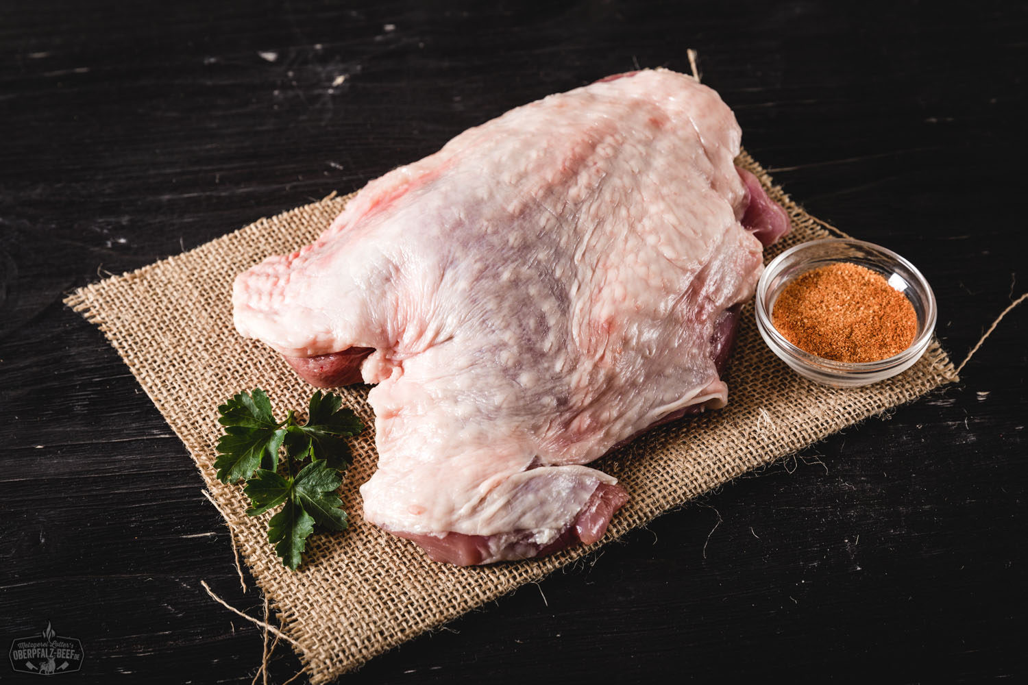 Rohe Putenoberkeule ohne Knochen auf einem Schneidebrett, umgeben von frischen Kräutern, Gewürzen und Knoblauchzehen – hochwertige Fleischzubereitung für Geflügelgerichte.