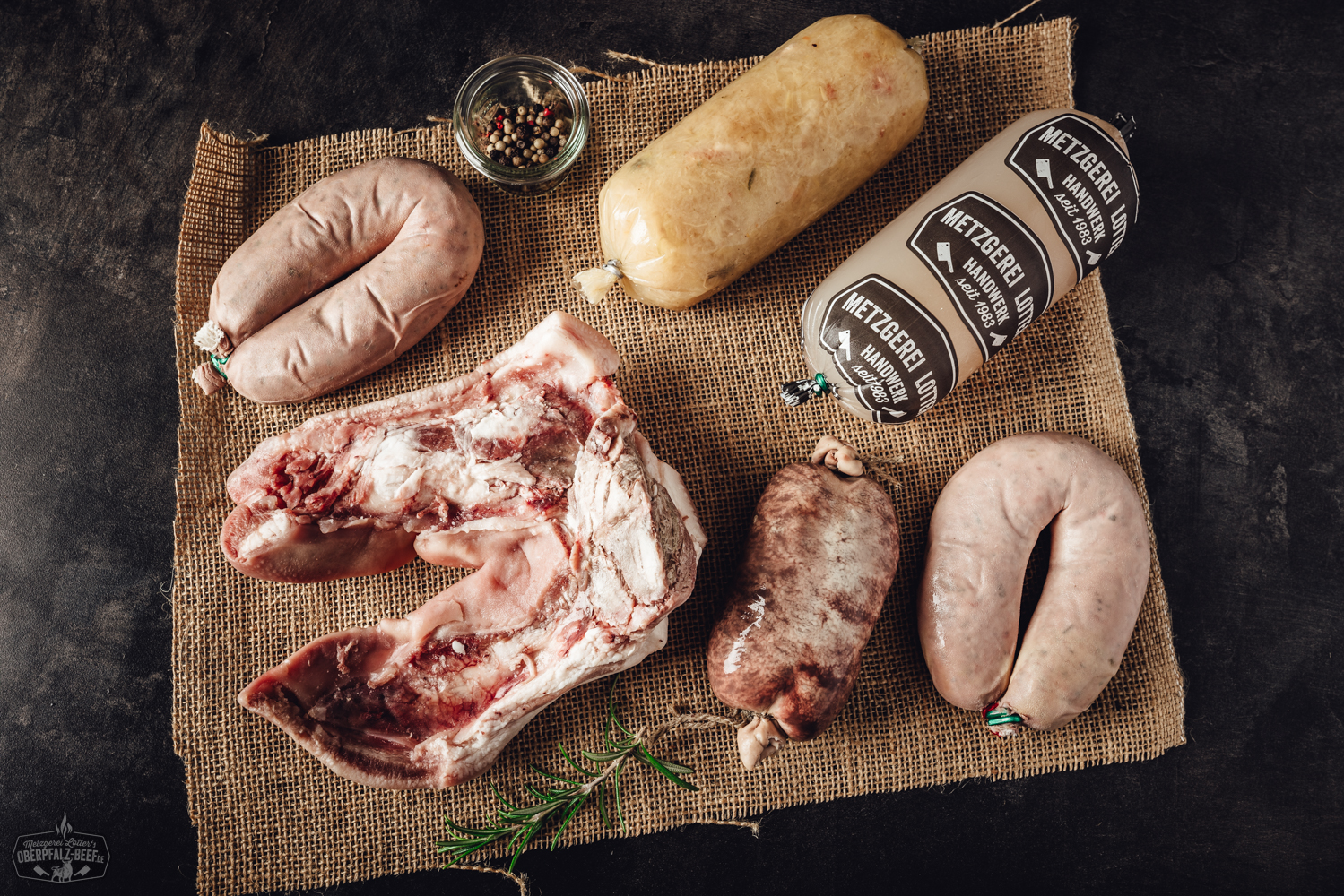 Schlachtschüssel-Platte Maxi – Bayerische Spezialitäten aus der Oberpfalz Gegarte Wildschweinhaxe vom Oberpfälzer Wild auf Holzbrett angerichtet, außen goldbraun und knusprig, umgeben von Rosmarinzweig, frischem Knoblauch und Pfefferkörnern – rustikale Fleischspezialität aus regionaler Jagd.