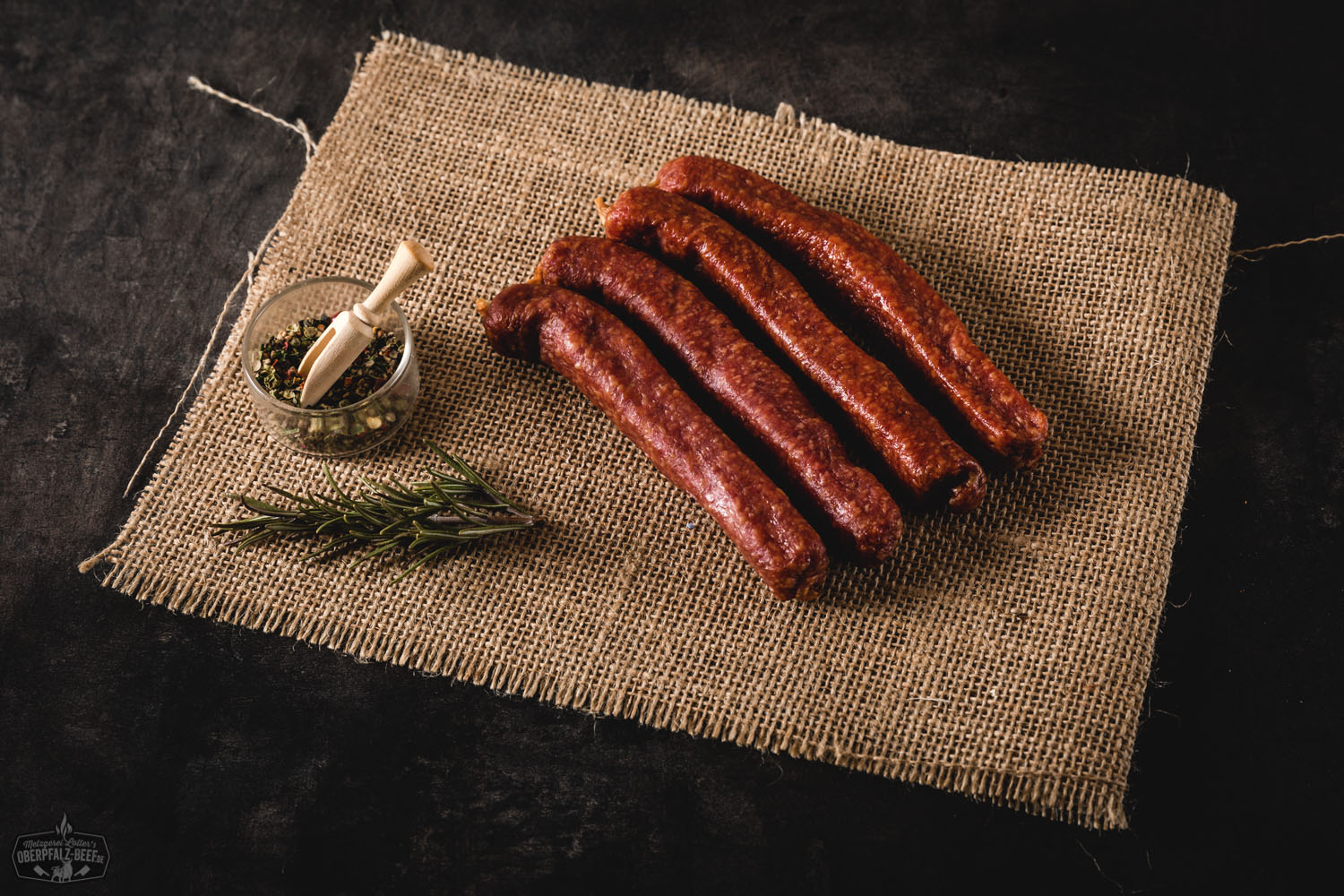 Traditioneller Landjäger aus der Oberpfalz – geräucherter Rohwurst-Klassiker Zwei traditionelle, dunkelrote Landjäger-Würste aus Rindfleisch hängen an einer Schnur vor rustikalem Holzhintergrund – Delikatess-Wurst aus der Oberpfalz, luftgetrocknet und herzhaft im Geschmack.