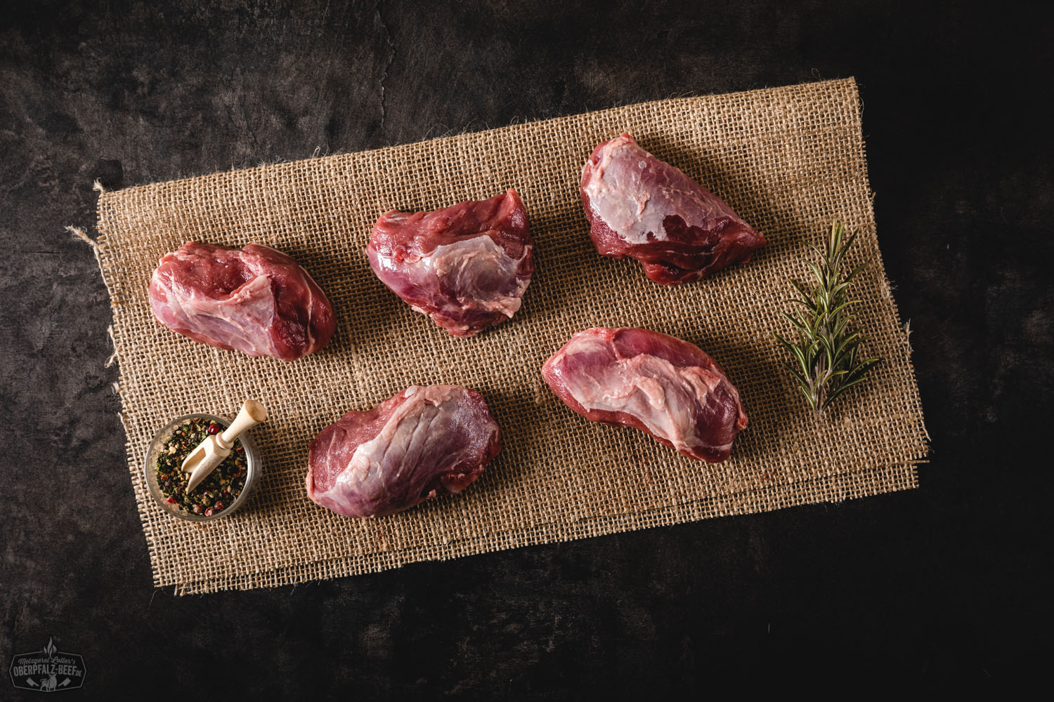 Schweinebäckchen vom Oberpfälzer Landschwein auf Holzbrett mit frischen Kräutern Zart geschmorte Schweinebäckchen vom Oberpfälzer Landschwein auf dunkel-glänzender Soße, serviert mit buntem Wurzelgemüse und Kartoffelpüree auf einem weißen Teller – rustikale, regionale Küche kunstvoll angerichtet.