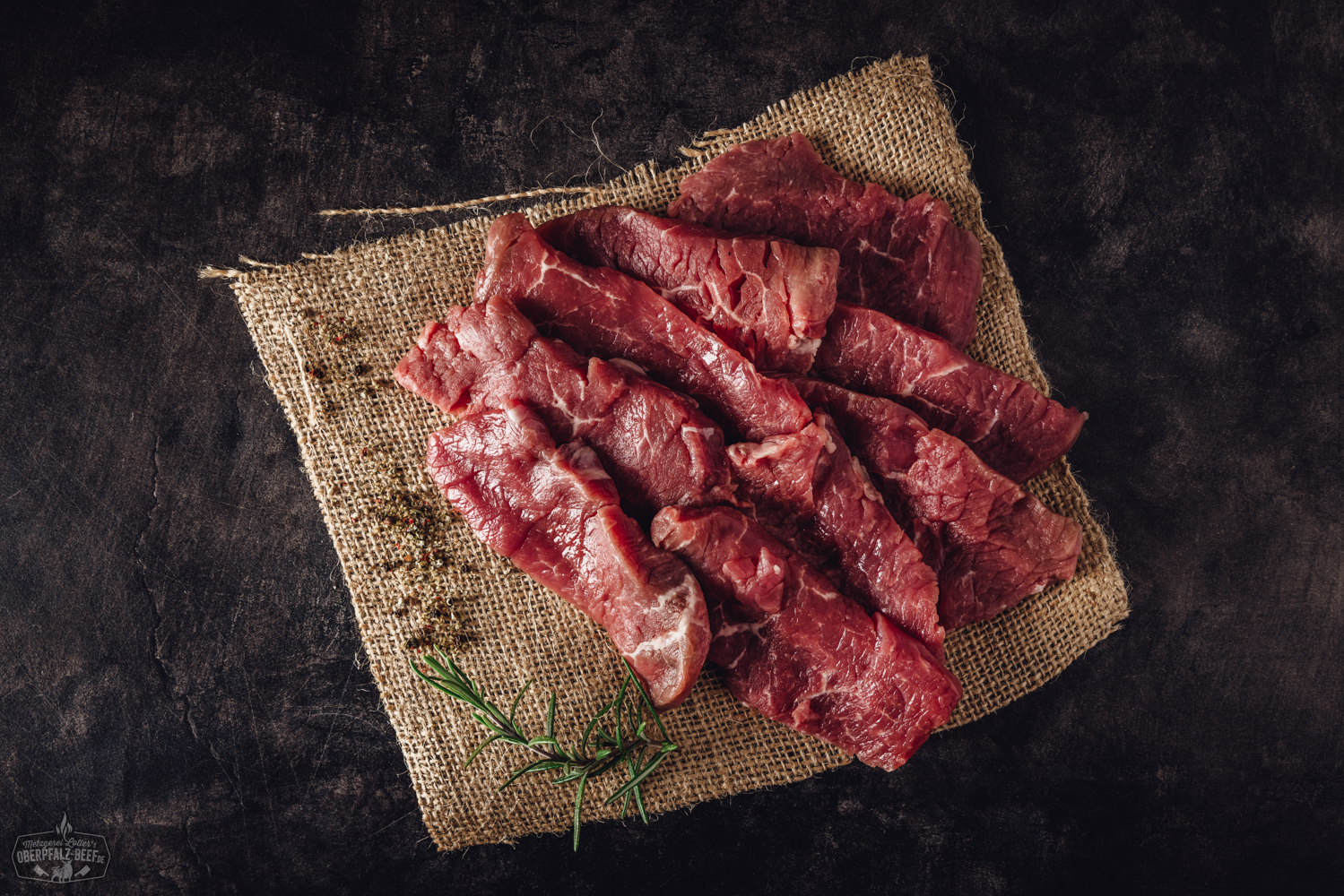 Handgeschnittenes Raclette-Fleisch aus Rinderfilet – hochwertiges Rindfleisch für Raclette und Grill Handgeschnittenes Rinderfilet für Raclette, roh und saftig auf einem dunklen Brett angerichtet, mit feiner Marmorierung und frischen Kräutern garniert – hochwertiges Beef aus der Oberpfalz.