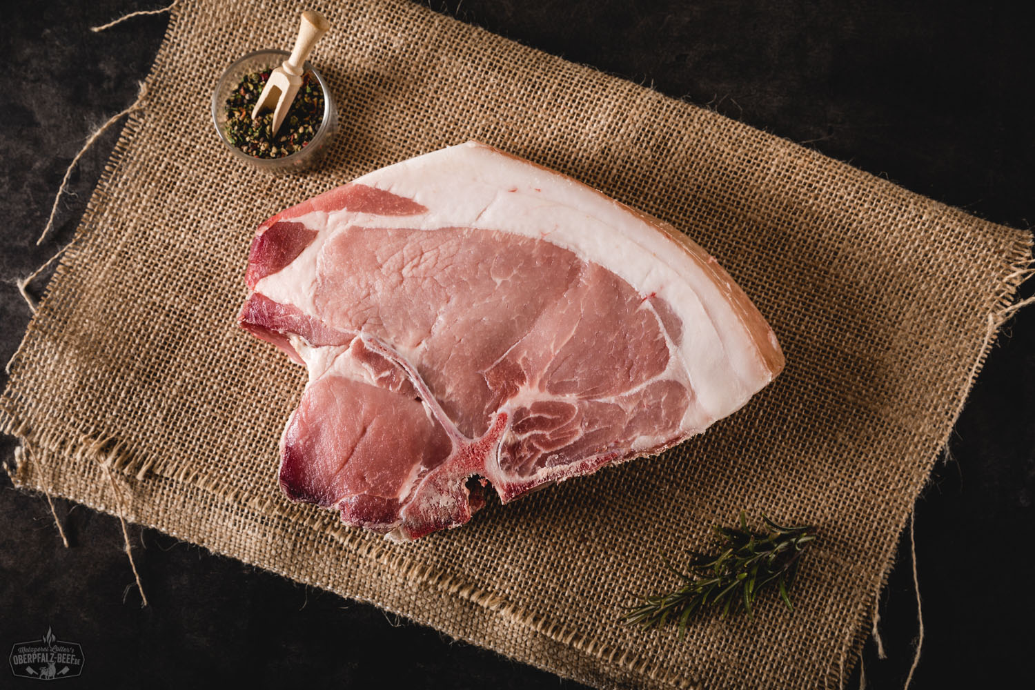 Dry Aged T-Bone Steak vom Oberpfälzer Landschwein – Premium Fleischqualität aus Bayern Rohes T-Bone-Steak vom Oberpfälzer Landschwein, dry-aged gereift, auf dunklem Untergrund, sichtbare Marmorierung und Knochenstruktur, hochwertiges Fleischstück für Steakliebhaber.