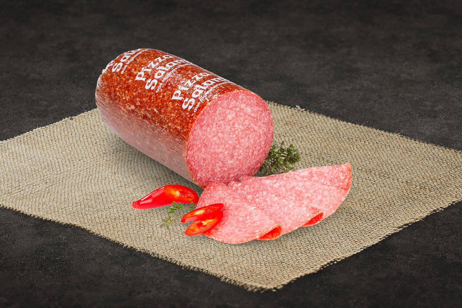 Geschnittene Pizzasalami – feine Scheiben für Pizza, Brotzeit und Antipasti Geschnittene Kürbiskernsalami auf einem Holzbrett, dekorativ angerichtet mit sichtbaren grünen Kürbiskernen in der Wurst; daneben frische Kräuter, Kürbiskerne und ein rustikales Messer – hochwertige Delikatesswurst aus der Oberpfalz.