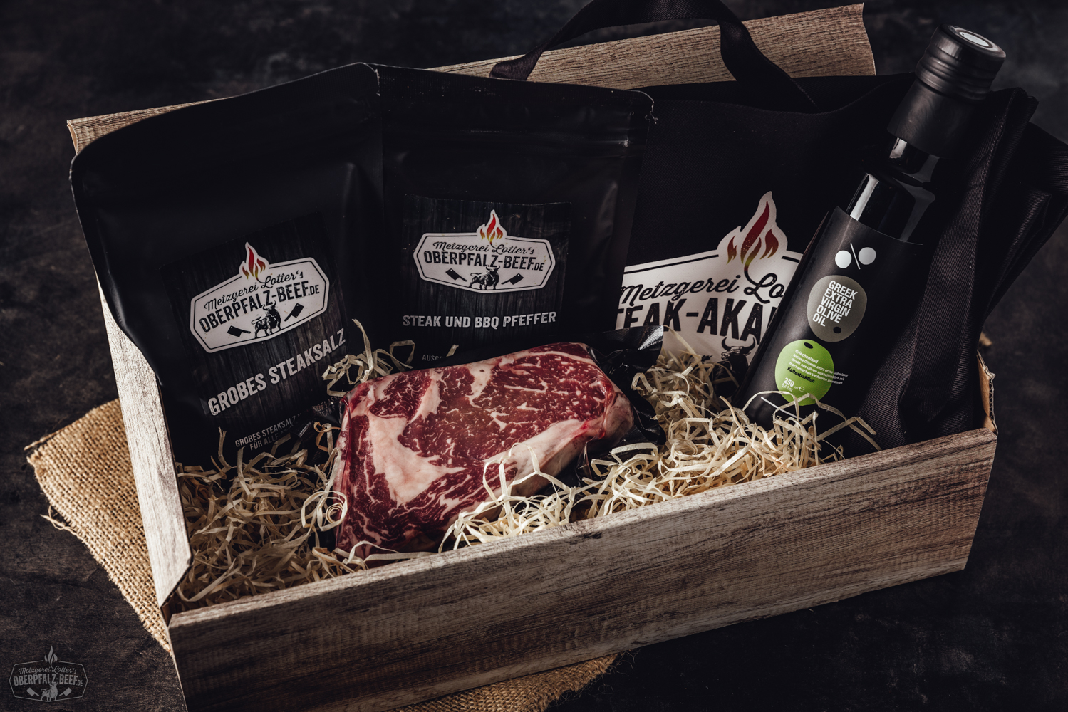 Grillpaket mit hochwertigem Rindfleisch: Verschiedene Stücke wie Steaks, Würste und Rippchen roh in einer schwarzen BBQ-Box auf Holzuntergrund angerichtet – frisches Premiumfleisch von Oberpfalz-Beef für Barbecue und Grillabend.