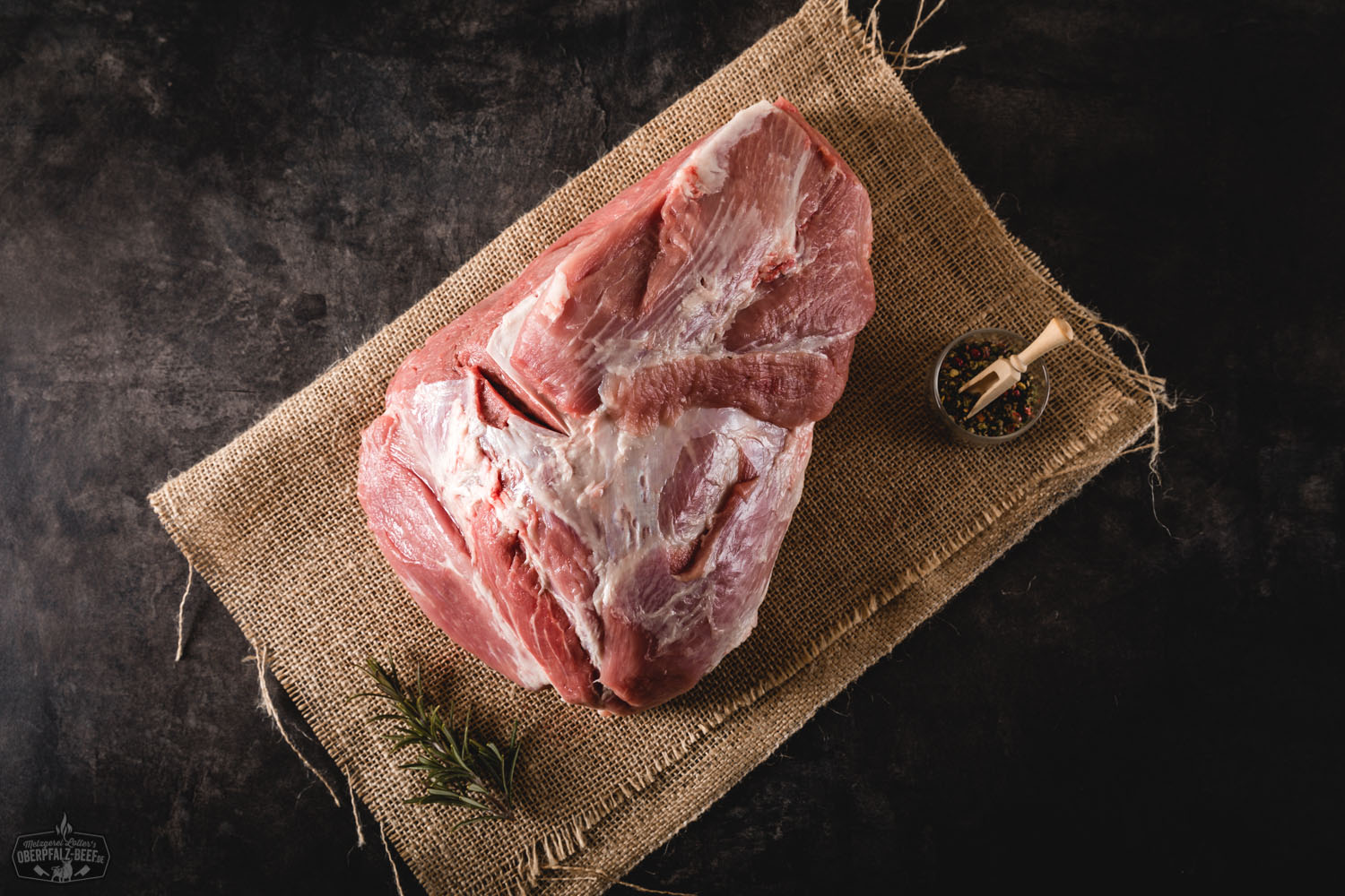 Roher Zuschnitt der dicken Schulter ohne Schwarte vom Oberpfälzer Landschwein auf Holzunterlage, mit sichtbarer Marmorierung und leichter Fettabdeckung, ideal für Braten oder Schmoren.