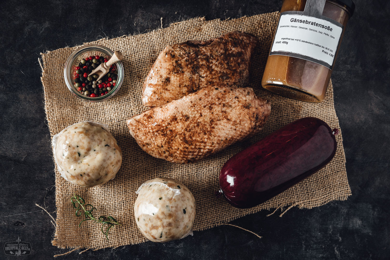 Rohes Gänsebrustfilet ohne Knochen auf Holzbrett, umgeben von Rosmarinzweigen, Pfefferkörnern und Knoblauchzehen – frische, regionale Zutat aus der Oberpfalz für festliche Bratenrezepte.