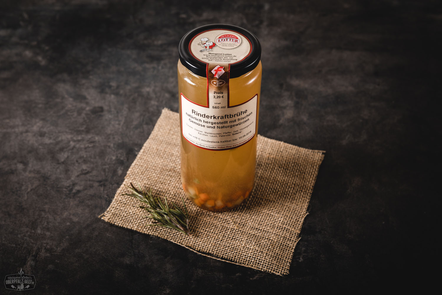 Ein verschlossenes Glas mit klarer Rinderkraftbrühe, goldbraun in der Farbe, steht auf einem dunklen Holzuntergrund; daneben liegen frische Kräuter, Meersalz und ein Löffel – hochwertige hausgemachte Rinderbrühe im Glas, traditionell und natürlich.