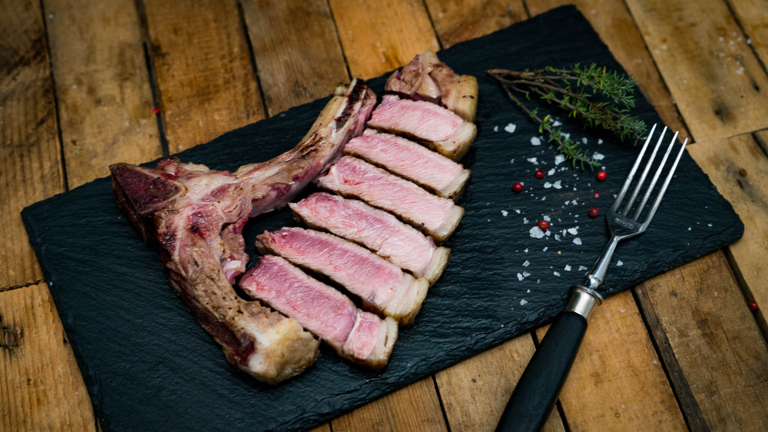 Kotelett vom Oberpfälzer Milchkalb frisch gegrillt auf Holzbrett serviert Rohes Kotelett vom Oberpfälzer Milchkalb mit hellem, zart marmoriertem Fleisch und kräftigem Knochenstück, appetitlich angerichtet auf dunkler Schieferplatte mit Gewürzen, Rosmarin und Knoblauch – hochwertige Delikatesse aus regionaler Aufzucht.