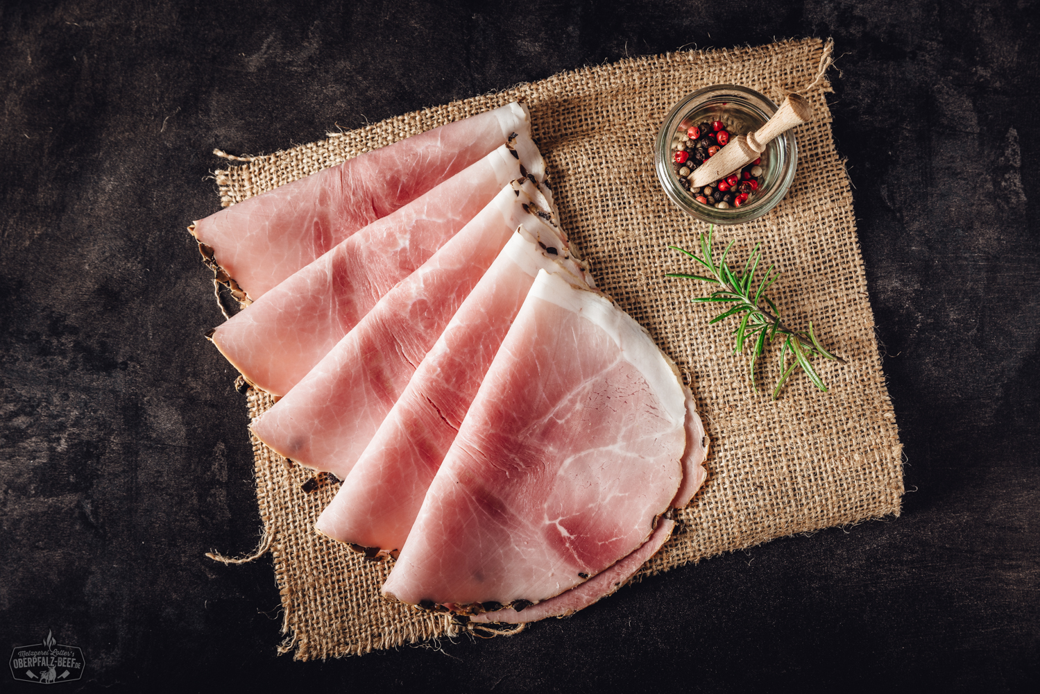 Trüffelschinken geschnitten – Delikatesser Schinken mit Trüffel Aroma Stadtwurst am Stück auf einem Holzbrett, angeschnitten, mit sichtbarer grober Fleischeinlage; daneben Senf, frische Petersilie und Gewürze – rustikale Präsentation bayerischer Wurstspezialität.