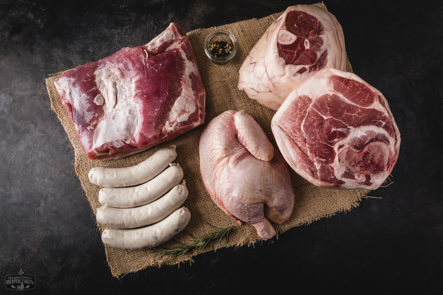 Oktoberfest Fleischpaket mit hochwertigem Rindfleisch – Frisch und regional aus der Oberpfalz Oktoberfestpaket mit hochwertigem Oberpfalz-Beef: Rohes Rindersteak, grobe Bratwürste, Rindfleischspieße und bayerisches Bier dekorativ auf Holzbrett angerichtet, umgeben von frischem Rosmarin und Brezeln – perfekte Fleischauswahl für Grill und Festtage.