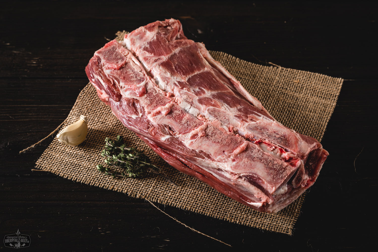 Rohes Lammhals-Stück mit Knochen vom Juradistl-Lamm auf dunklem Untergrund, saftig marmoriert, frisch zugeschnitten – ideales Fleischstück für Schmoren oder Braten.