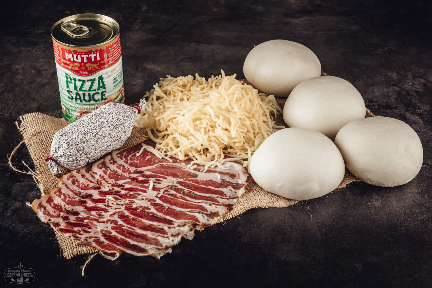 Pizza-Paket „Hot“ mit scharfen Zutaten: Rohes Grill-Paket mit feurig belegten Mini-Pizzen, Rindfleisch, Peperoni, Jalapeños, Chiliwurst und Grillzubehör auf schwarzem Untergrund, hochwertig verpackt – ideal für BBQ und Grillfans.