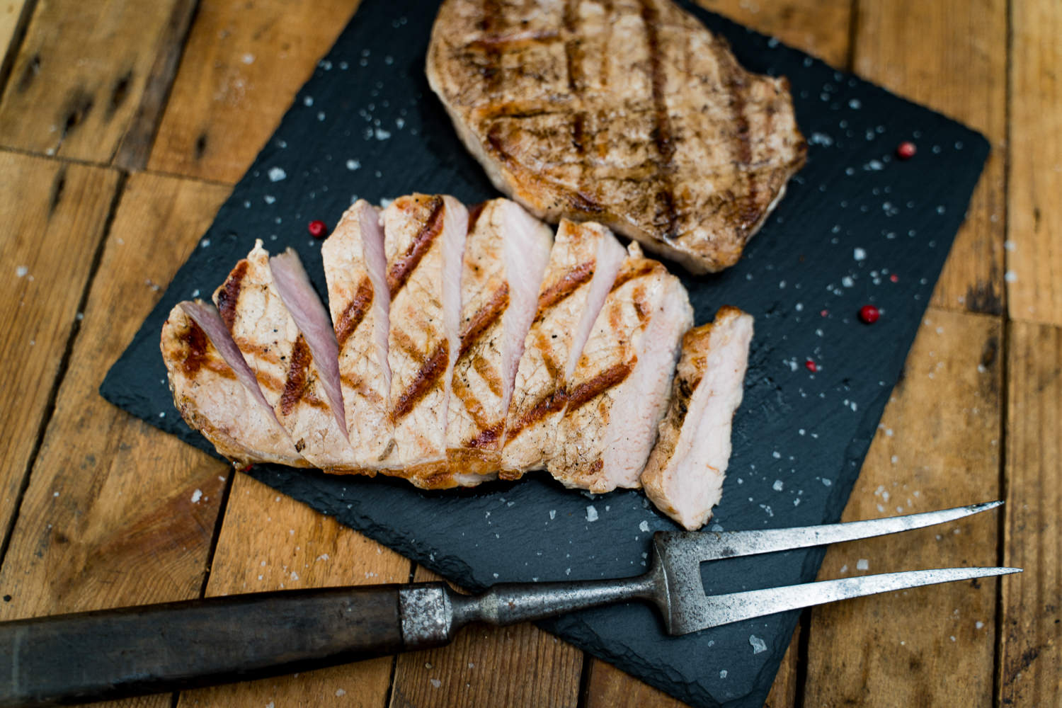 Gewürzte Rückensteaks vom Oberpfälzer Landschwein – regionales Schweinefleisch in hoher Qualität Drei gewürzte Rückensteaks vom Oberpfälzer Landschwein roh auf Holzbrett angerichtet, mit Pfeffer, Salz und Gewürzen bestreut; rustikale Präsentation für Grill- oder Fleischliebhaber.