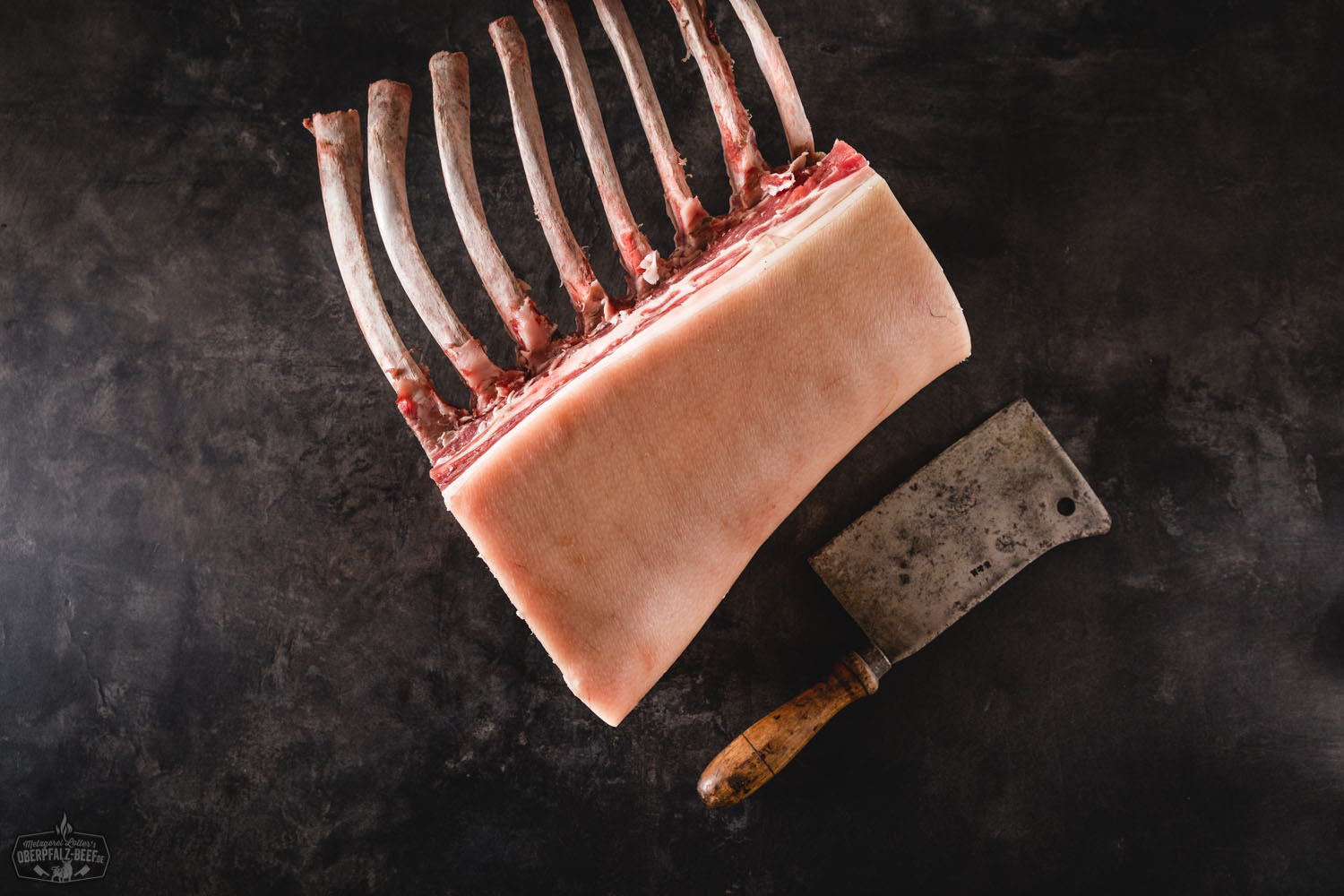 Dry Aged Tomahawk Kotelett vom Oberpfälzer Landschwein – Halbes Stück in Premiumqualität Halbes Dry-Aged Kotelett im Tomahawk-Cut vom Oberpfälzer Landschwein auf dunklem Untergrund, roh mit sichtbarer Marmorierung und langem Rippenknochen – hochwertiges Schweinefleisch für Steak-Zubereitung.